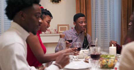 The festive table is set for Christmas as multi-ethnic friends pray, holding hands with closed eyes while a guy in a shirt says the prayer. Later, a student gave a toast, prompting everyone to raise