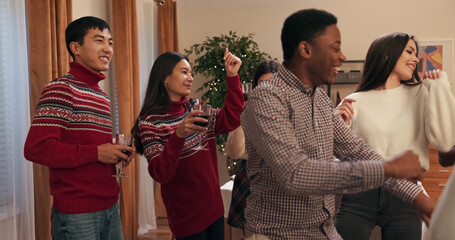 After their session, students gathered to celebrate. Festively dressed, they are dancing and chatting. The friends are holding glasses of wine, smiling, and having fun in the room with music and
