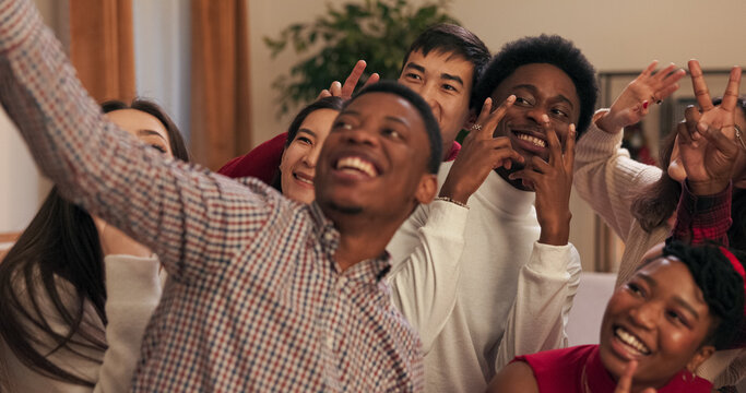 Close-up of friends taking selfie. Guy in checkered shirt is holding phone and taking pictures. Students pose and smile. Boys and girls having fun and chatting at party.