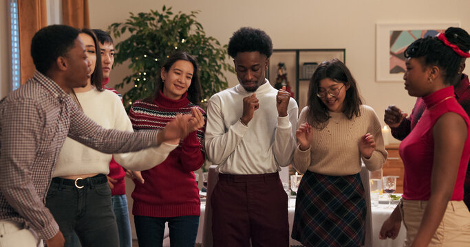Students celebrate the end of the session by dancing at a party. A multi-ethnic guy in a shirt pulls out a phone to take a selfie with friends. Boys and girls are posing.
