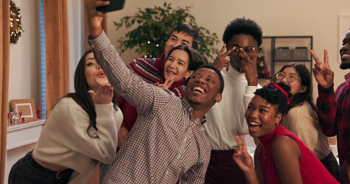 Friends are posing for a selfie taken by a multi-ethnic guy in a shirt, who pulls a phone from his pocket. The students are dancing at a party to celebrate the end of the session.