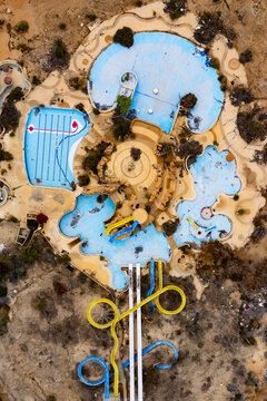 Aerial view of abandoned water park with faded blue pools shaped like cartoon characters amidst dry, cracked earth, a haunting scene of forgotten leisure, The Dead Sea, South District, Israel.