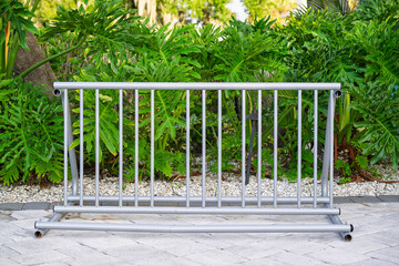 A silver bike rack stands ready on smooth stone pavers, framed by a lush wall of vibrant green vegetation in the background.
