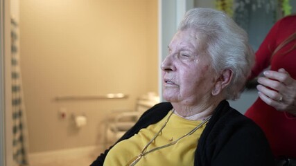 An elderly woman receives gentle care and grooming from a staff member in a home healthcare facility, showcasing kindness and support.
