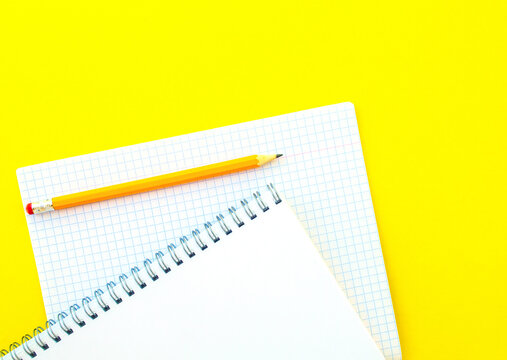 White notebook with spring, checkered notebook and pencil.