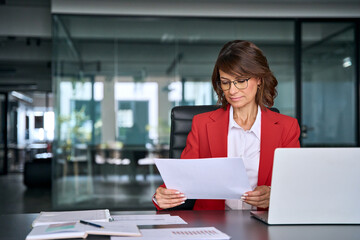 Focused business woman saleswoman working on laptop computer reading analysing financial loan contract document in office. Mature manager businesswoman specialist doing paperwork using pc. Copy space