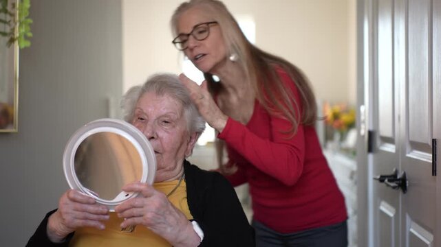 An elderly woman in a healthcare facility receives care and attention while looking at herself in a mirror during personal grooming.
