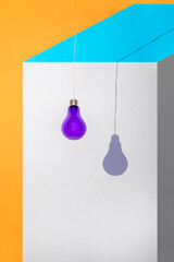 Geometric still life with purple light bulb on wire and shadow