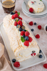 Meringue Pavlova roll cake with cream and fresh berries on top on a ceramic board on a concrete background. Copy space.