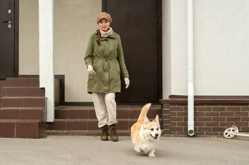 Woman walks with her dog welsh corgi outdoors. Stylish lady enjoys playtime whith her pet. Autumn season. Fall time.