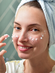 Beautiful Young Woman applying facial moisturizing cream in bathroom.Home interior. Skincare concept