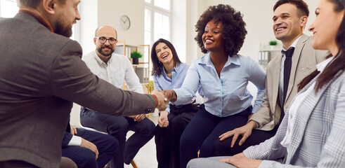 Multinational business team is conducting a meeting in the office, sitting in a circle. Colleagues are shaking hands, symbolizing agreement and teamwork. Collaborative spirit among team members.