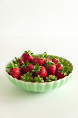 Fresh red strawberries in a green bowl on white table. Front view