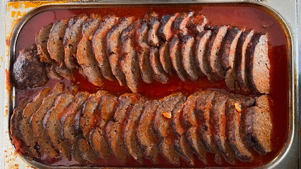 Ready to serve, arranged in two rows, slices of juicy roast in tomato sauce.