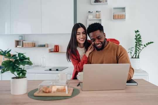 Diverse couple using laptop at home kitchen