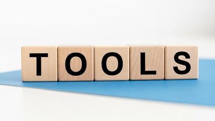 Wooden blocks spelling out the word tools on a blue surface against a white background in a studio shot