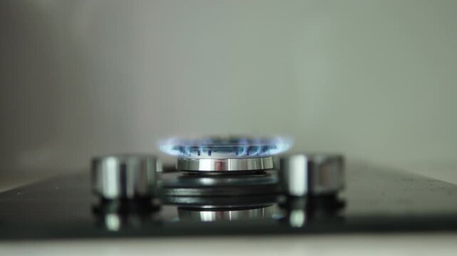 Hand turns knob of modern gas stove and shuts off natural gas supply. Blue flame of burner dims and disappears. End of cooking and energy consumption due to tariffs.