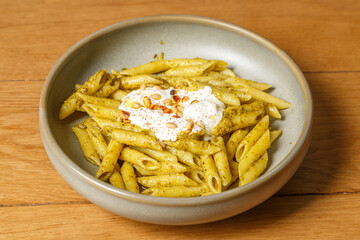 Penne (pâtes) au pistou et stracciatella, parsemés de pignons de pin sur une table en bois
