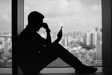 silhouette man stressed while looking at phone by window