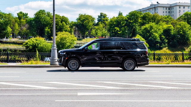 Fast moving Cadillac Escalade on the city road. Black SUV with man driving. Premium auto in fast motion with blurred background. Speeding in the city concept