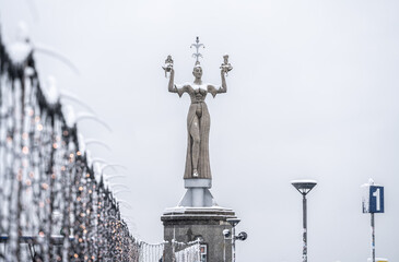 View across the pier decorated with Christmas lights to the snow-covered Imperia statue at the harbor, which is covered in falling snow. Constance, Baden W&uuml;rttemberg, Germany.