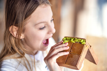 Young pretty girl eating tasty milk dubai chocolate with pistachio cream. Woman enjoying sweet trendy chocolate dessert. Dubai pistachio chocolate with kadayif.