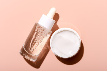 Glass dropper bottle and cream jar on a soft pink background,