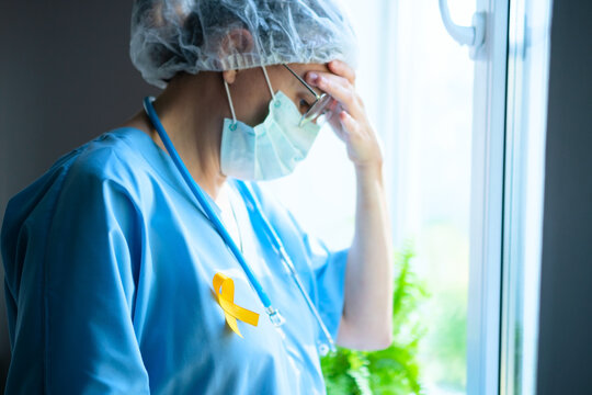 A weary woman medical staff with yellow satin ribbon on uniform deeply thinks about patient treatment, showing hard medical work.