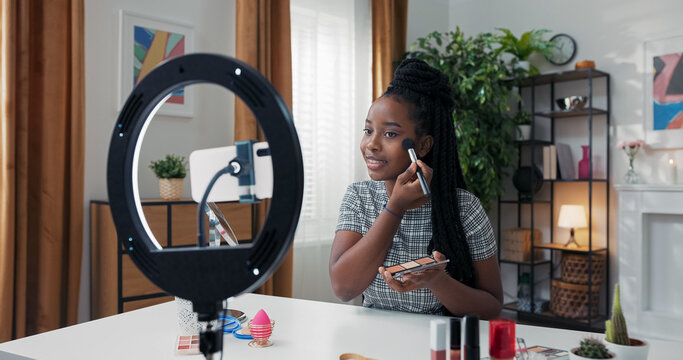 Influencer creates beauty content at home, teaching followers how to use bronzer and highlighter. She carefully defines her cheekbones and blends products into her skin.