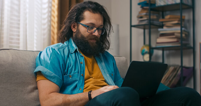 A casually dressed man works from the couch with a laptop, writing emails, preparing complaints, and completing paperwork from home.