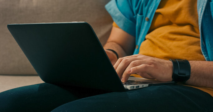 A relaxed man with a beard and glasses types on a laptop placed on his lap, completing digital paperwork and submitting online forms.