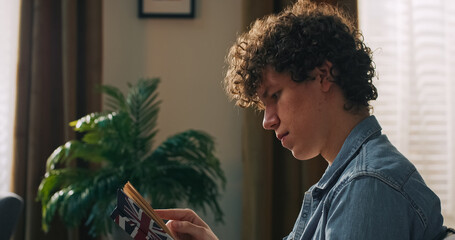 A frustrated teenager sits on the sofa with an open book, reflecting on difficult material while...