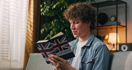 A focused boy studies language at home, holding an English dictionary and reviewing new vocabulary in his thoughts. © ABCreative