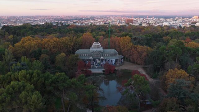 Aerial view of the Crystal Palace surrounded by vibrant autumn trees and a reflecting pond, a lush oasis amidst the urban skyline, Madrid, Community of Madrid, Spain.