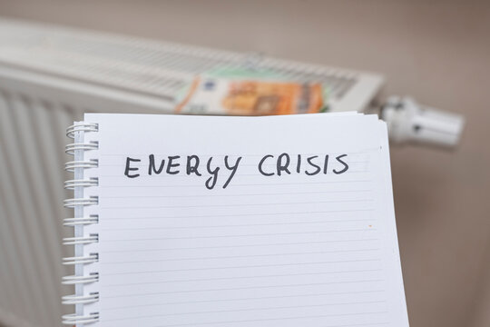 Handwritten note stating energy crisis placed on table next to radiator, highlighting the impact of rising energy costs in modern households and providing a call to action.