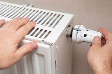 A person adjusting the thermostat on a white radiator, ensuring comfortable indoor climate control at home. This scene reflects maintenance and home improvement.