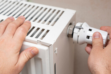 A person adjusting the thermostat on a heating radiator, demonstrating the importance of climate control and energy efficiency in a home environment.