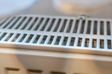 Close-up of a white air vent cover placed on a heating unit, showcasing its slotted design. This detail is common in home and office environments for ventilation.