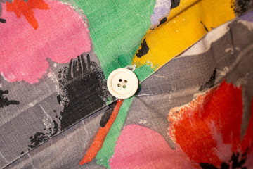 Close-up of a vibrant, multicolored fabric featuring artistic floral patterns, showcasing a white button, ideal for fashion, textile design, or home decor applications.