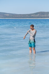 Man Applying Mud on His Body While Standing in Shallow Water of a Tranquil Beach During a Sunny Day