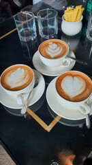 Three cups of perfectly crafted latte art coffee with elegant designs, served on a dark reflective table in a cozy cafe setting.