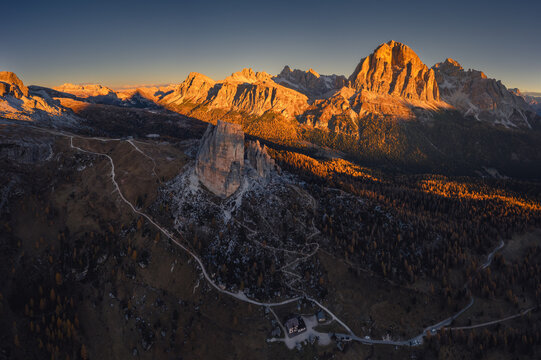 Autumn morning near Cinque Torri and Tofana in the Dolomites — drone view of golden light, crisp air, and rugged peaks above quiet valleys. A serene, colorful mountain landscape.