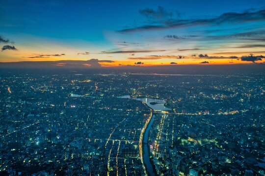 Aerial view of a sprawling cityscape illuminated by the fading embers of sunset, the river snaking through the urban tapestry, Dhaka, Dhaka Division, Bangladesh.
