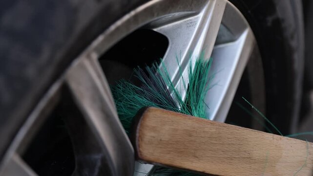 Specialist cleans car wheel from dust and dirt using special brush. Technician performs maintaining tasks of automobile cleanliness during final stage of repair works in service center