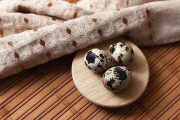 Three quail eggs on a round wooden plate placed on a wooden surface with a linen napkin. Concept of natural nutrition, organic food, eco products, rustic cooking and healthy lifestyle.