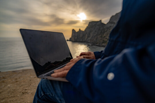 Remote work laptop travel digital nomad typing outdoors near stunning sea cliffs at sunset