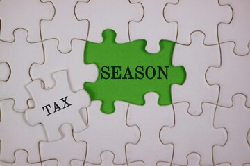 Fototapeta premium Close-up of puzzle pieces, featuring a bright green piece labeled SEASON beside a white piece labeled TAX. Symbolizes the link between tax season and personal or business finances.