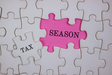 Fototapeta premium Close-up of puzzle pieces, featuring a pink piece labeled SEASON beside a white piece labeled TAX. Symbolizes the link between tax season and personal or business finances.