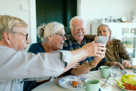 Senior friends laughing while sharing a smartphone at home