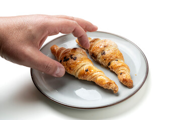 Hand reaching for chocolate chip pastry croissants on plate